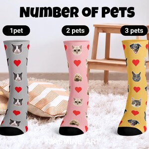 May include: Three pairs of knee-high socks with pet-themed designs. One pair is gray with cat faces and red hearts, another is pink with cat and dog faces and red hearts, and the third is yellow with dog and cat faces and red hearts. The text "NUMBER OF PETS" is at the top.