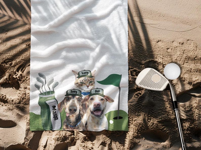 May include: White golf towel featuring a whimsical design with a cat and two dogs wearing golf hats, with the names "Lucy", "Zoey", and "Gus" printed on the hats. A golf club and ball are also visible.