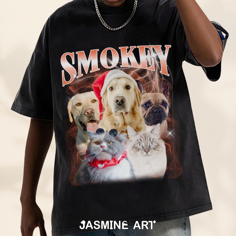 Op de afbeelding: Zwart T-shirt met een grafische print van vijf dieren. De dieren zijn een golden retriever met een kerstmanmuts, een Franse bulldog, een golden retriever, een kat met een zonnebril en een kat. De tekst "SMOKEY" is in oranje en rode letters boven de dieren gedrukt. De tekst "JASMINE ART." is in witte letters onderaan het T-shirt gedrukt.