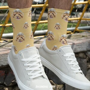 May include: A pair of white sneakers with a yellow and brown patterned socks featuring a dog wearing a hat. The socks are crew socks and the sneakers are low-top.