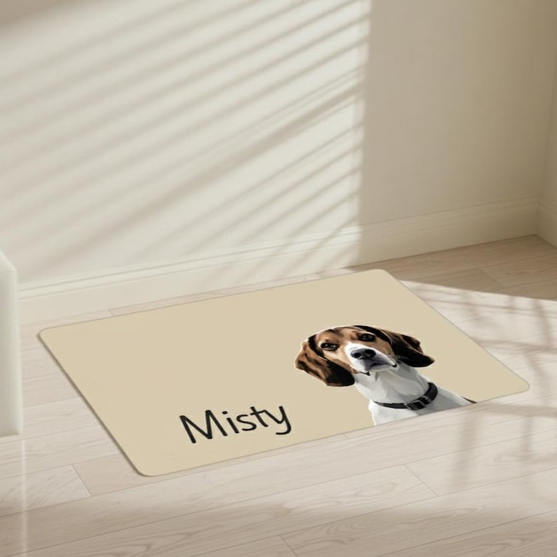 May include: A rectangular beige mat featuring a dog portrait with brown and white fur, wearing a black collar. The name "Misty" is printed in black. The mat is placed on a light wood floor.