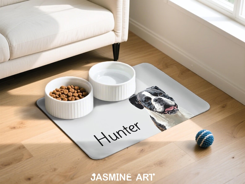May include: A dog-themed pet feeding station featuring a light gray placemat with a dog portrait and the name "Hunter". Includes two white ceramic bowls, one filled with kibble, and a blue and white ball.