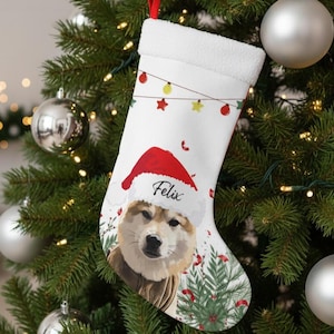 May include: White Christmas stocking with a festive design featuring a dog wearing a Santa hat. The stocking has the name "Felix" printed on it, and is decorated with string lights and Christmas tree elements.