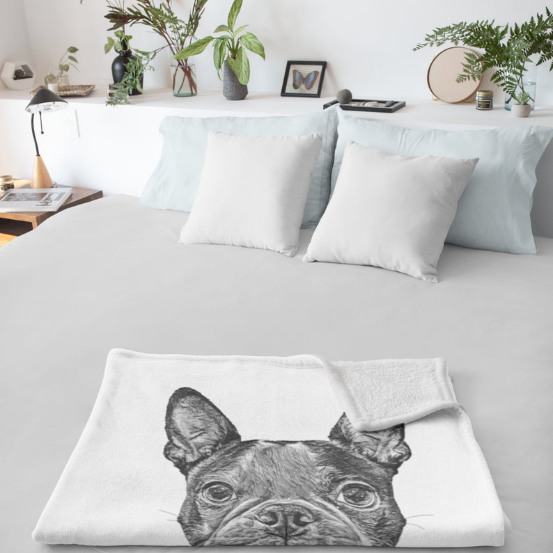 May include: A white fleece throw blanket with a black and white illustration of a French Bulldog peeking out from behind the blanket.