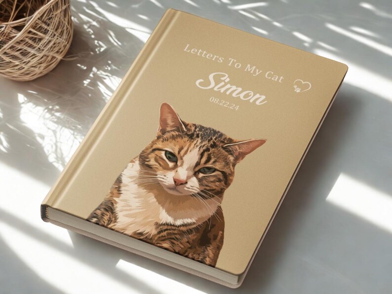Pode incluir: Um di&aacute;rio de capa dura com um retrato de gato na capa. O t&iacute;tulo &eacute; "Letters To My Cat", com o nome "Simon" e a data "08.22.24". O gato &eacute; retratado em tons de castanho, branco e bege, com um s&iacute;mbolo de cora&ccedil;&atilde;o.