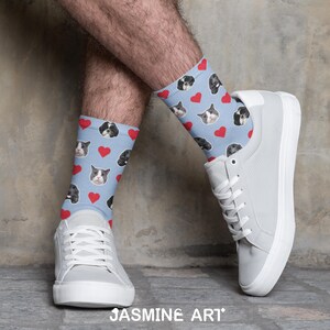 May include: Light blue socks with a pattern of dog faces and red hearts. The socks are worn with white sneakers. The image is set against a neutral background. The socks are a fun and unique accessory.