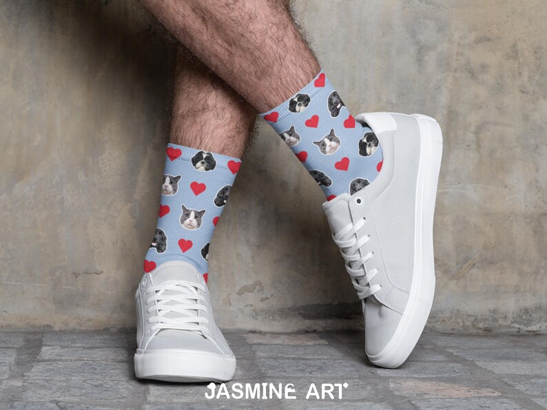 May include: Light blue socks with a pattern of dog faces and red hearts. The socks are worn with white sneakers. The image is set against a neutral background. The socks are a fun and unique accessory.