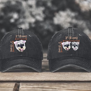 May include: Two black baseball caps featuring embroidered Schnauzer dog portraits. The left cap shows a single dog head measuring 2 inches by 2 inches. The right cap displays two dog heads measuring 3 inches wide by 2 inches high.