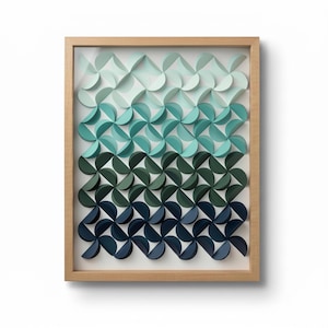 Pode incluir: Uma peça de arte de parede emoldurada com um padrão geométrico repetitivo de semicírculos de papel dobrado. O design exibe um gradiente de cor vertical que transita do verde menta claro no topo para o azul marinho profundo na base, em uma moldura de madeira clara.