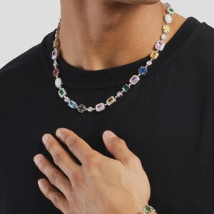May include: A silver necklace and bracelet set featuring a series of colorful, rectangular gemstones. The gemstones are set in a silver chain, with a variety of colors including pink, green, yellow, and blue. The bracelet is on the wrist.