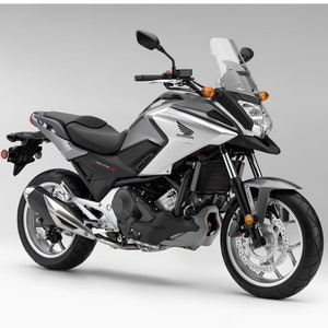 Op de afbeelding: Een zilveren en zwarte Honda motorfiets met een windscherm en een zwart zadel. De motorfiets heeft een zilveren uitlaatpijp en zwarte wielen.