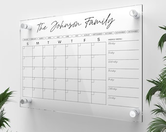 May include: A clear acrylic dry erase calendar with a black frame and the text "The Johnson Family" at the top. The calendar includes a monthly grid with spaces for each day of the week and a section for a weekly menu.