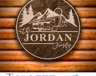 May include: A round wooden sign with a brown woodgrain finish. The sign features a silhouette of a camper van driving through a mountain landscape with trees. The text "The Jordan Family" is written below the camper van.