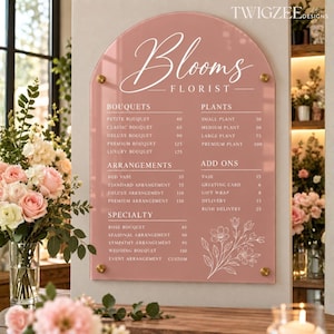 May include: An arched, dusty rose acrylic sign for Blooms Florist featuring white text and line art. The menu lists categories including Bouquets, Plants, Arrangements, Add Ons, and Specialty with prices. It is mounted with four gold-toned hardware standoffs.