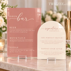 May include: A rectangular dusty rose acrylic open bar sign with white text and a matching arched cream acrylic signature cocktails sign with rose-colored text, both displayed on clear acrylic stands on a marble surface.