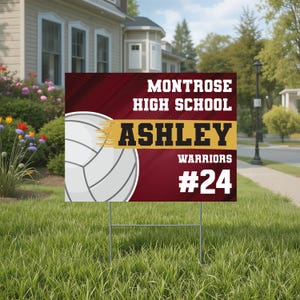 May include: A rectangular yard sign with a maroon background featuring a white volleyball graphic. The text reads MONTROSE HIGH SCHOOL, ASHLEY in black on a gold horizontal bar, WARRIORS, and #24 in white. The sign is supported by a metal wire frame.