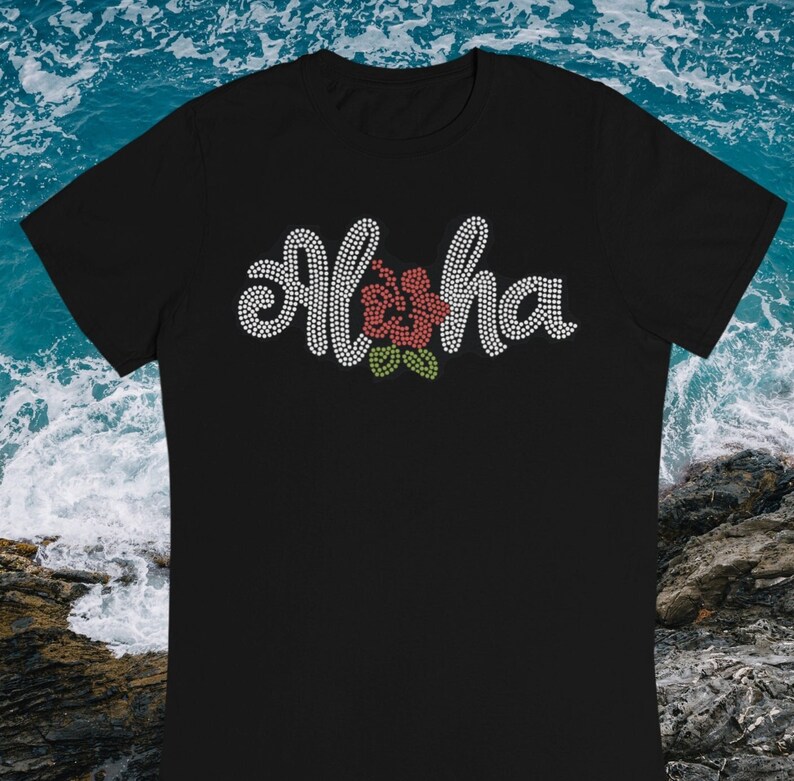 May include: Black t-shirt with a white rhinestone design that says "Aloha" with a red hibiscus flower in the center.