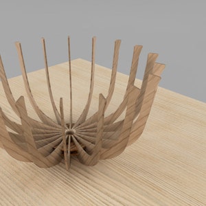 May include: A wooden bowl made of thin strips of wood that are curved and joined together to form a bowl shape. The bowl is empty and is sitting on a wooden surface.