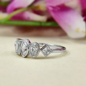 May include: A silver ring featuring five clear gemstones of varying shapes. The ring is displayed against a white backdrop.