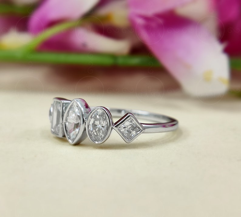 May include: A silver ring featuring five clear gemstones of varying shapes. The ring is displayed against a white backdrop.