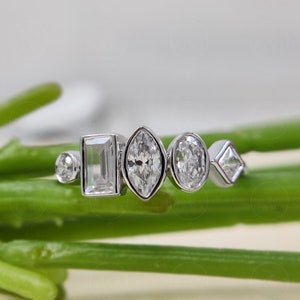 May include: A silver ring with five different shaped clear gemstones. The ring is on a green stem.