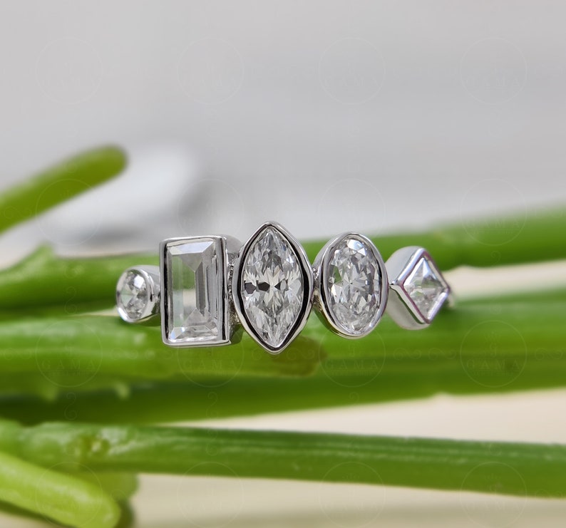 May include: A silver ring with five different shaped clear gemstones. The ring is on a green stem.