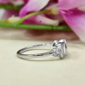 May include: A silver ring featuring three clear gemstones. The central stone is a rectangular emerald cut, while the two side stones are round brilliant cuts.