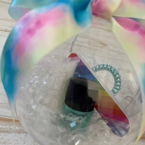 Puede incluir: Un globo de pl&aacute;stico transparente lleno de relleno blanco iridiscente, que contiene una lima de u&ntilde;as de arco&iacute;ris, una botella transparente de esmalte de u&ntilde;as con tapa negra y un tubo de brillo de labios etiquetado como "Sugar Kisses Gloss".