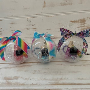 Puede incluir: Tres adornos de pl&aacute;stico transparente llenos de confeti de colores, purpurina y peque&ntilde;os regalos. Cada adorno est&aacute; decorado con una cinta diferente: arco&iacute;ris, tie-dye y estampado de leopardo.