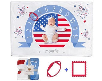 May include: A white milestone blanket featuring a red, white, and blue American flag circle, numbers 1 through 12, and fireworks graphics. Includes a folded blanket, a red football-shaped marker, and a red square frame for tracking months.