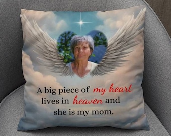 May include: Square pillow with a printed image of a woman's portrait inside a heart-shaped design with angel wings. The text reads: "A big piece of my heart lives in heaven and she is my mom."