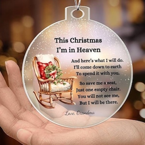 May include: Clear Christmas ornament with the text "This Christmas I'm in Heaven" and a poem. The ornament features a rocking chair with a Christmas stocking and wreath. A silver string is attached for hanging.