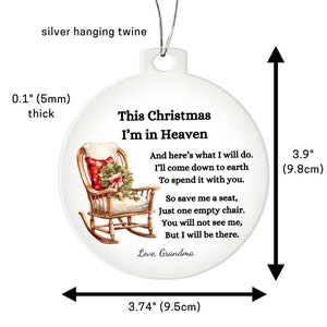 May include: A round Christmas ornament with a silver hanging twine. The ornament features a rocking chair with a red and white plaid pillow and a Christmas wreath. Text reads "This Christmas I'm in Heaven." The ornament is 3.9 inches (9.8cm) tall and 3.74 inches (9.5cm) wide.