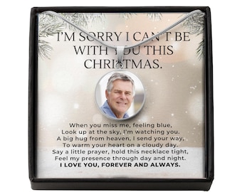 Op de afbeelding: Een zilveren ketting met een ronde hanger met een foto van een man. De hanger wordt gepresenteerd in een zwarte doos met de tekst "I'M SORRY I CAN'T BE WITH YOU THIS CHRISTMAS."