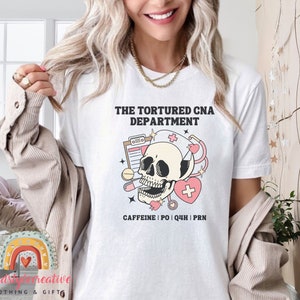 May include: White t-shirt with a skull wearing a nurse's hat and stethoscope. The text reads "The Tortured CNA Department" and "Caffeine | PO | Q4H | PRN".