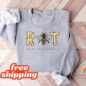 May include: Gray sweatshirt with the text "RBT" in yellow and black with a bee graphic. The text below the letters reads "Registered Behavior Technician".