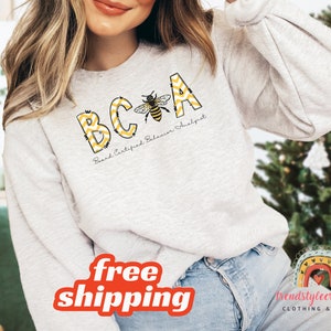 May include: A grey sweatshirt with a bee design and the text "BCA Board Certified Behaviour Analyst".