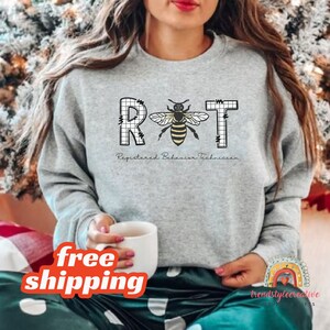 May include: A gray sweatshirt with the text "RBT Registered Behavior Technician" and a bee graphic. The bee is in a grid pattern.