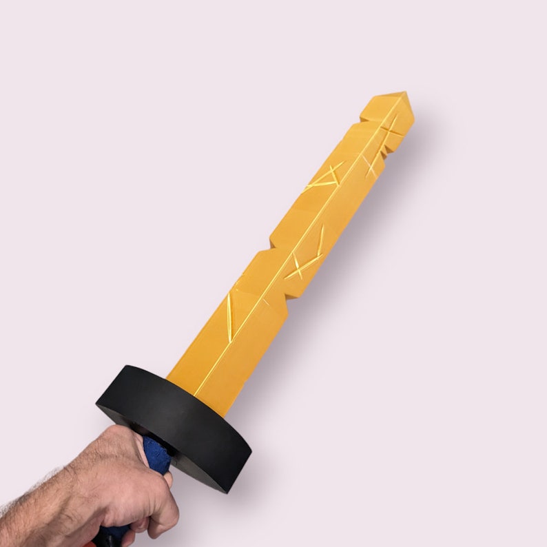 May include: A gold-colored toy sword with a black handle. The sword has a textured surface and a pointed tip.