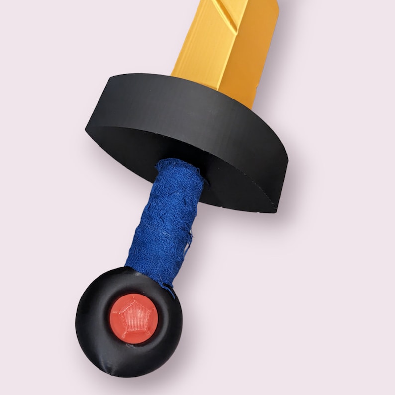 May include: A black and gold toy sword with a blue fabric handle and a red button on the end.
