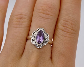 May include: A silver ring with an ornate design featuring a marquise-shaped amethyst gemstone.