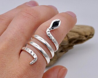 May include: A silver snake ring with a black enamel head. The ring is coiled around the finger and has a textured design.