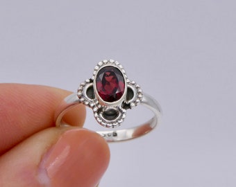 May include: A silver ring with a red gemstone set in a decorative, ornate design.