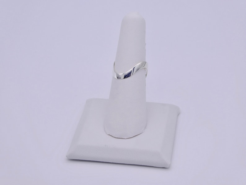 May include: A silver-colored ring with a V-shaped design. The ring is displayed on a white ring holder. The ring's smooth, polished surface reflects light, highlighting its elegant, minimalist style. The ring is a piece of jewelry.