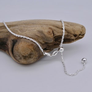 May include: A silver rope chain necklace with an adjustable sliding clasp. The chain is made of a twisted rope design and has a small silver bead at the end of the slider.