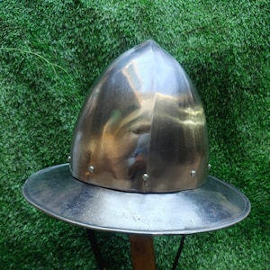 May include: A silver helmet with a wide brim and a pointed top. The helmet is on a wooden stand.