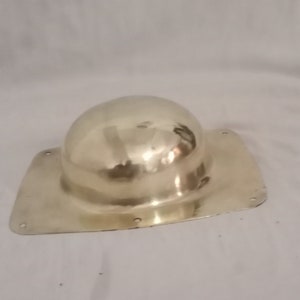 Op de afbeelding: Een glanzend, goudkleurig metalen object met een afgeronde koepelvorm op een rechthoekige basis. De basis heeft kleine gaatjes langs de randen. Het object reflecteert licht, wat wijst op een gepolijst oppervlak. Het lijkt een decoratief of functioneel item te zijn.