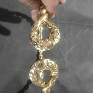 May include: A gold-colored necklace with two ornate circular pendants. The necklace is made of twisted rope-like metal.