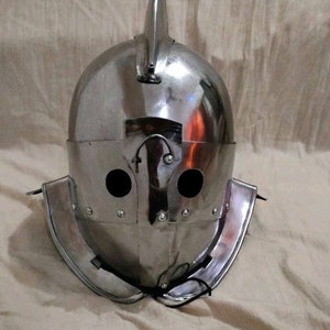 May include: A silver helmet with a pointed crest and two eye holes. The helmet has a neck guard and a chin strap.