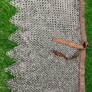 May include: A silver chainmail skirt with a brown leather trim. The skirt is made of interlocking metal rings and has a scalloped edge.